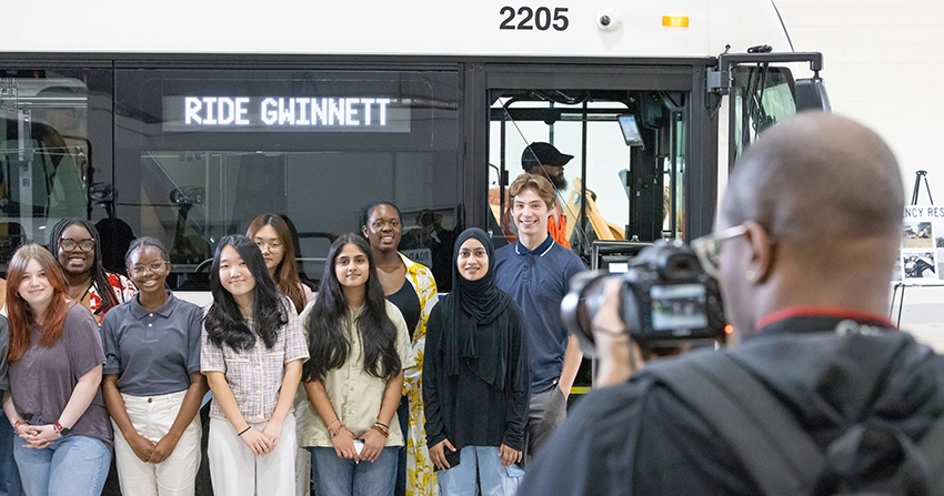 Group of youth smiling in front of camera man and a Ride Gwinnett bus